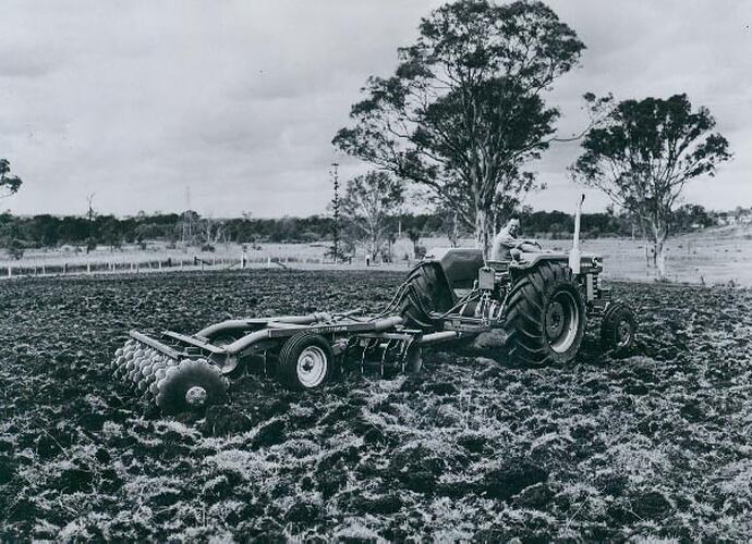 Right hand side view of a tractor coupled to a harrowin a ploughed field.
