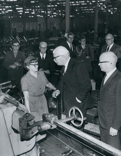 Group of men talking to woman in factory.