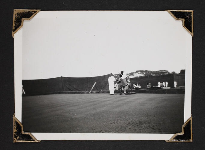 Men playing lawn bowls, with tarp fencing in background.