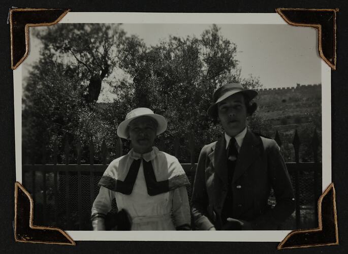 Two woman in uniform with fence and trees behind.