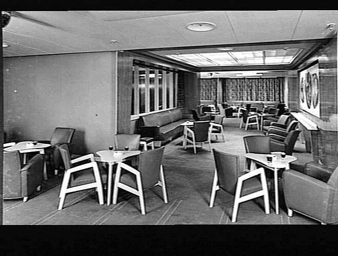 Ship interior. Room with upholstered chairs around tables and some armchairs set up to be a cafe area.