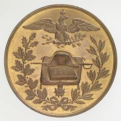 Round bronze medal with Napoleon's hat, sword and book on a cushion. Wreath below, crowned eagle above.