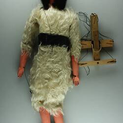 Back of male marionette, cream fur tunic. Black hair and beard. Wooden handle, strings attached.