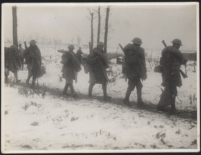 Six soldiers walking along a track in a snow covered landscape.