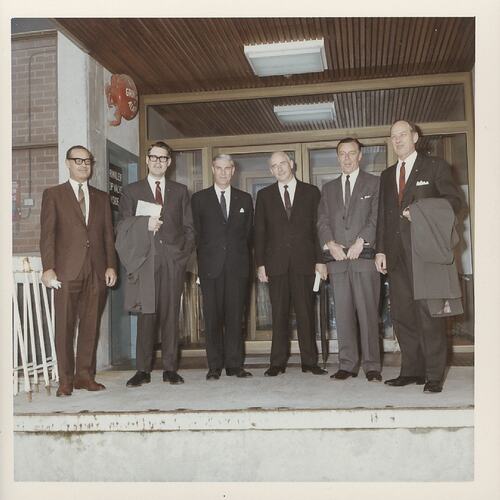 Six men in suits on concrete stoop.