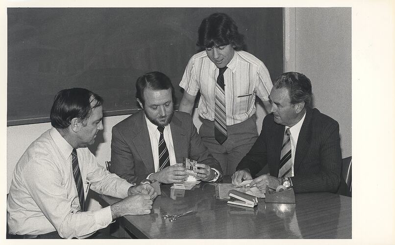 Four men looking at photographic packaging.