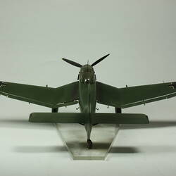 Model aeroplane. Dark green with black cross on wing tips. Black propeller. Back view.