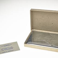 Silver metal cigarette case in card box. Has etched outline map of Australia on lid.