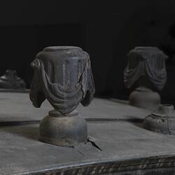 Black wooden hearse, detail of decorative woodwork. Urns with draped cloth.