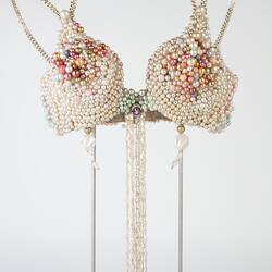 Cream pearl brassiere with pink and blue beads. Gold chain neck, shoulder straps. Pearl strands at centre.