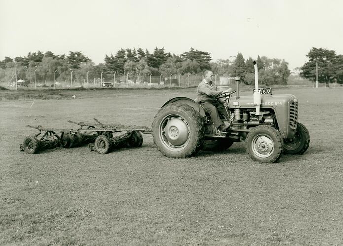 Man driving a tractor towing a rotary gang mower on a sports or park ground.