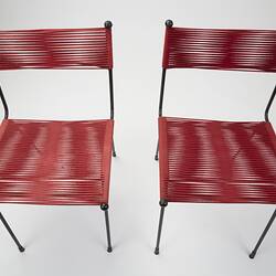 Two metal chairs strung with red cord seats and back sections. Top centre view.