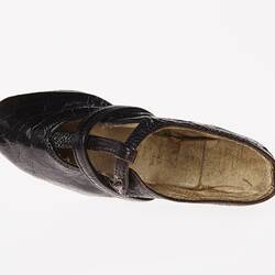Miniature hand-sewn black leather shoe with strap and glass button fastener. View from top.