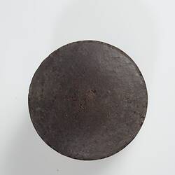 Disc-shaped dark brown briquette with flat sides. Top view.