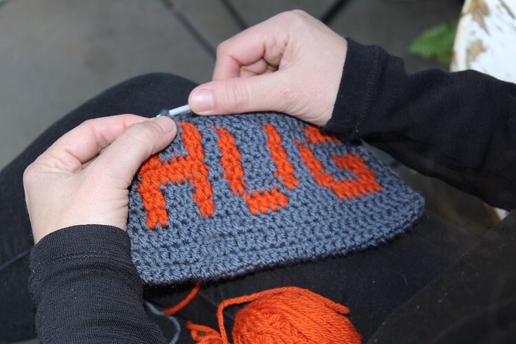 Womans hands crocheting rectangle reading 'HUG'.