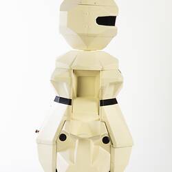 Side view of cream plastic robot with angular human-like shape, ie. head, shoulders, waist and legs. Black plastic features.