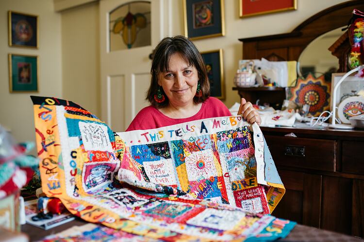 Woman sitting at table holding colourful quilt.