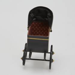 Painted black metal miniature pram with gold painted highlights and folding leather hood. Front.