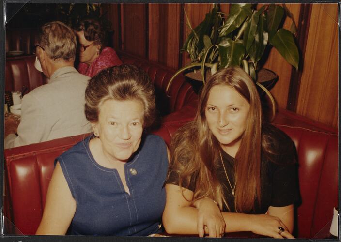 Two women posing in a red booth seat.