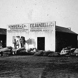 Negative - Men with Camel & Chaff Sacks in Front of Shed for Kimber & Co, Timber Merchants, & F.E. Randall & Co, Forage & Produce Merchants, Western Australia (?), circa 1905