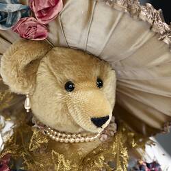 Detail of light brown teddy bear wearing lavish cream hat.