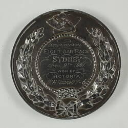 Round medal with engraved text within wreath border.