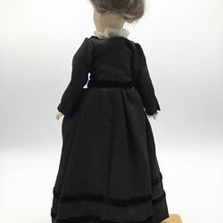 A doll dressed in a dark brown dress with a cameo brooch