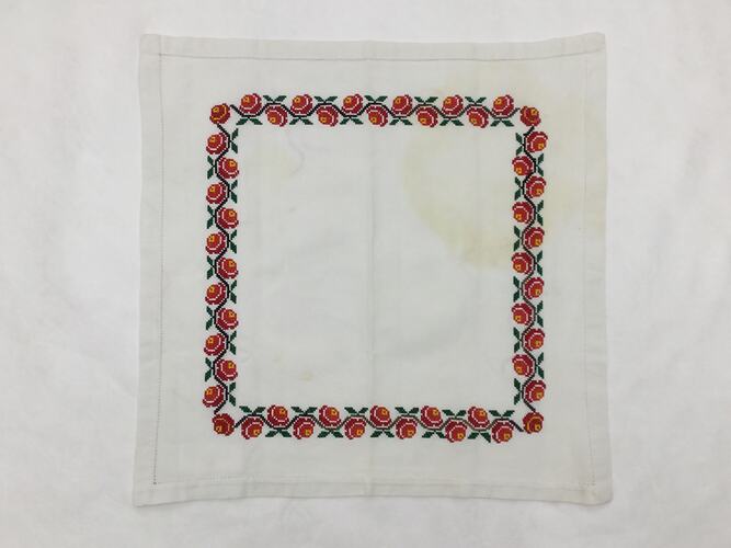 Off-white square cloth embroidered with an inset square margin of red roses with green leaves.