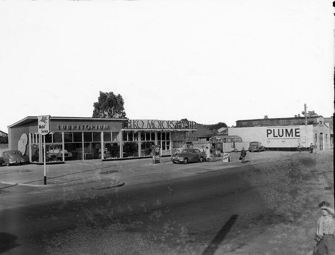Mobil garage with shop and service area. Male attendant refuelling a Bristol motor car. Motor bus in behind.