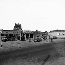 Mobil garage with shop and service area. Male attendant refuelling a Bristol motor car. Motor bus in behind.