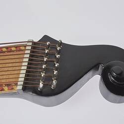 Detail of timber stringed instrument. Pale wood neck with zig zag pattern on edges. Stylised curved black laquered head stock. 61 strings in varied thickness.