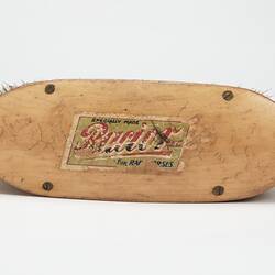 Oval shaped light brown wooden brush with off-white bristles. Label on top.
