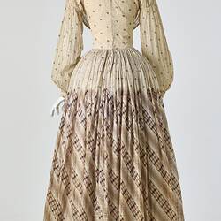 Cream muslin dress, high neck, long sleeves, banded waist, full length gathered skirt. Bustle. Back