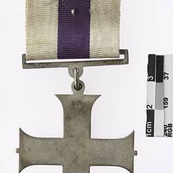 Silver cross shaped medal with white and purple ribbon.