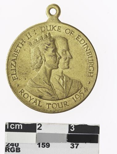 Round gold coloured medal with profile of a and crowned woman, text surrounding.
