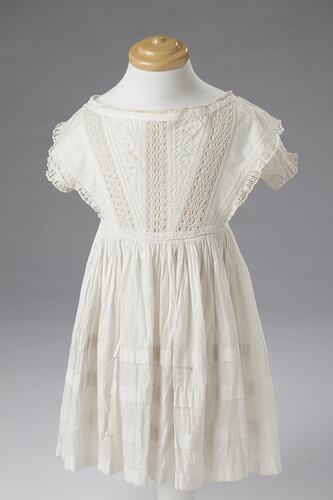 Short sleeved white cotton and lace girls dress. Three strips of lace down front.