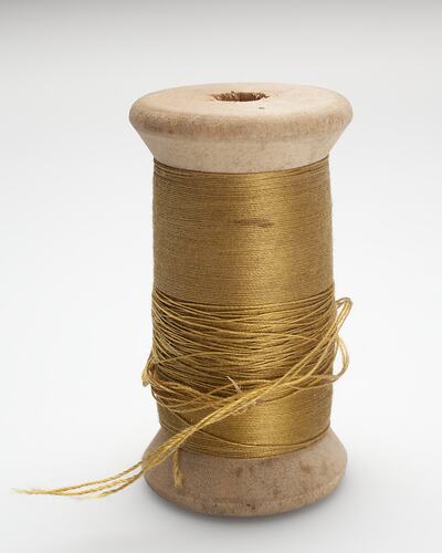 Wood cotton reel wound with gold cotton.