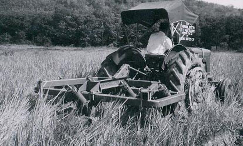 Man driving a tractor though a field of grass with a tiller attached.