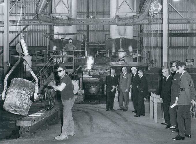 Group of men observe foundry workman.