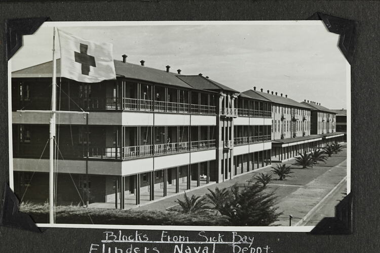 Exterior of row of three-story buildings and flag with cross in left foreground