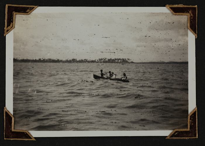 Five people in a row boat, with land in background.