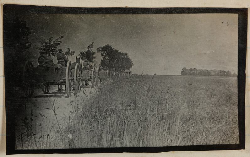View of horsedrawn carts travelling on a road next to a field.