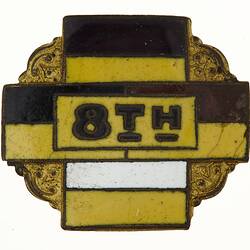 Enamel badge with yellow, black and white cross and black text.