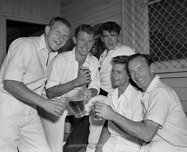 Five men in cricket clothing drinking beer.