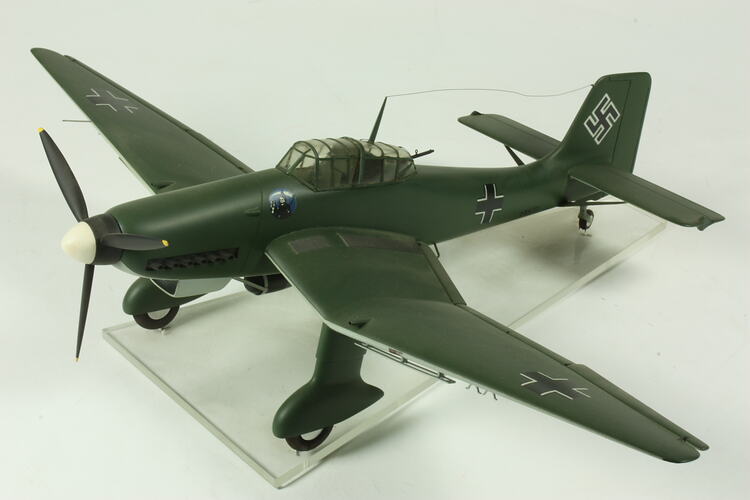 Model aeroplane. Dark green with black cross on side, wing tips and tail. Black propeller.