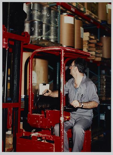 Man wearing overalls and driving a red forklift.