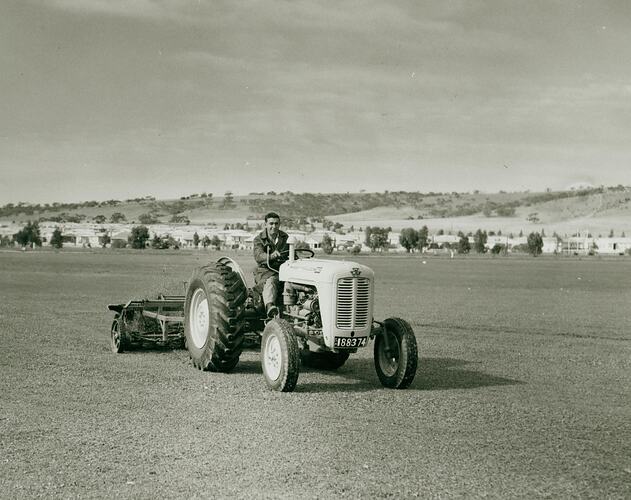 Man driving at tractor towing a tandem mower in a large open short cut grass field.