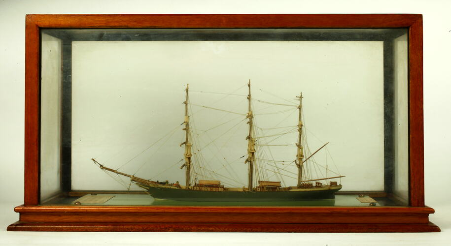 Model clipper sailing ship with three masts. House in wooden framed glass box.