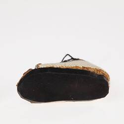 Miniature white canvas prosthetic shoe. Black rubber sole. View from below.