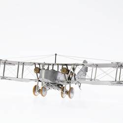 Model of a bi-plane made mostly of aluminium sheet metal. It has two pairs of wheels at front. Front view.